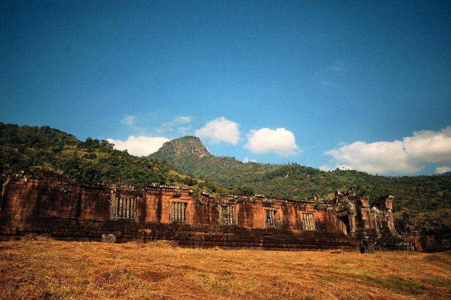 Ruines du temple khmer Vat Phou à Champasak, entourées de montagnes et de rizières dorées.