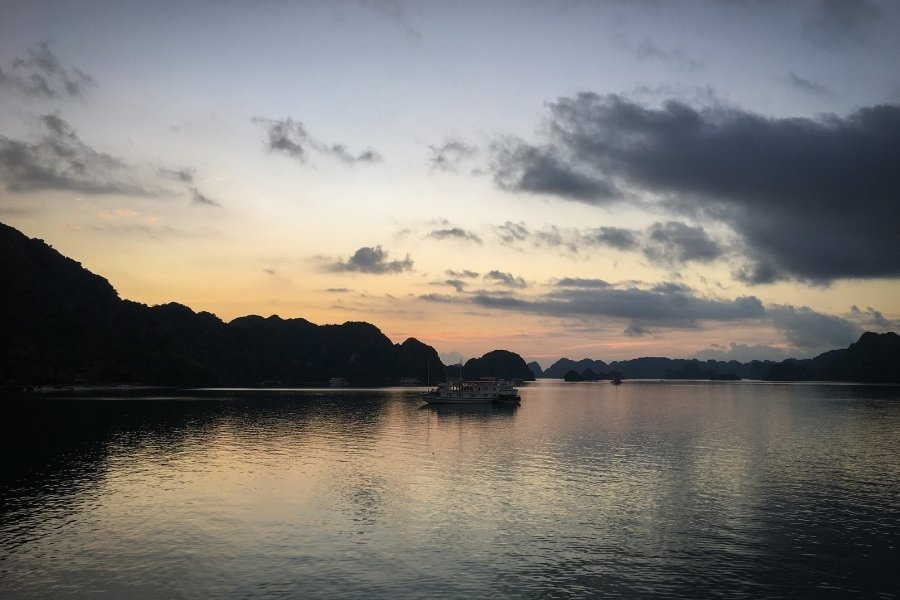 Îlots karstiques de la baie d'Ha Long sous un ciel doré, avec des jonques ancrées sur l'eau émeraude.