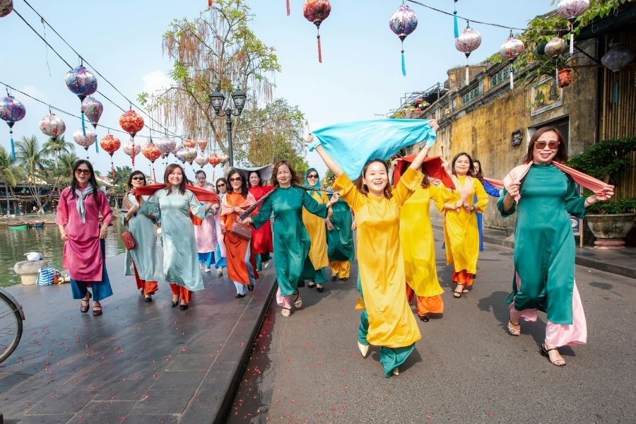 Femmes portant un ao dai traditionnel vietnamien, avec des lignes fluides et des motifs délicats, dans une rue de Hoi An.